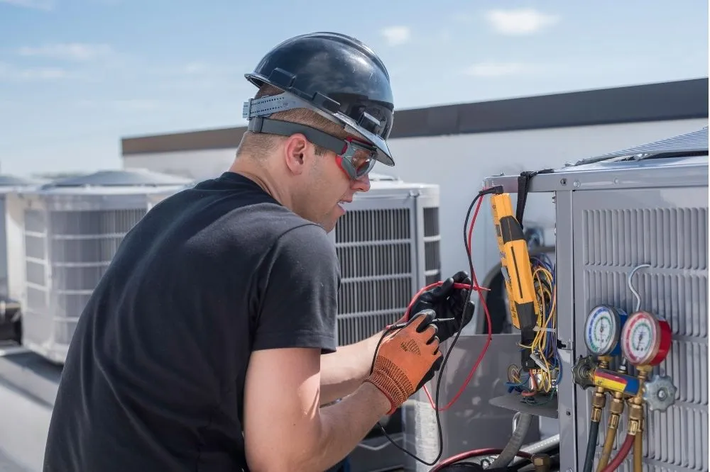 An HVAC expert is on top of a roof testing electrical connections on a furnace replacement.